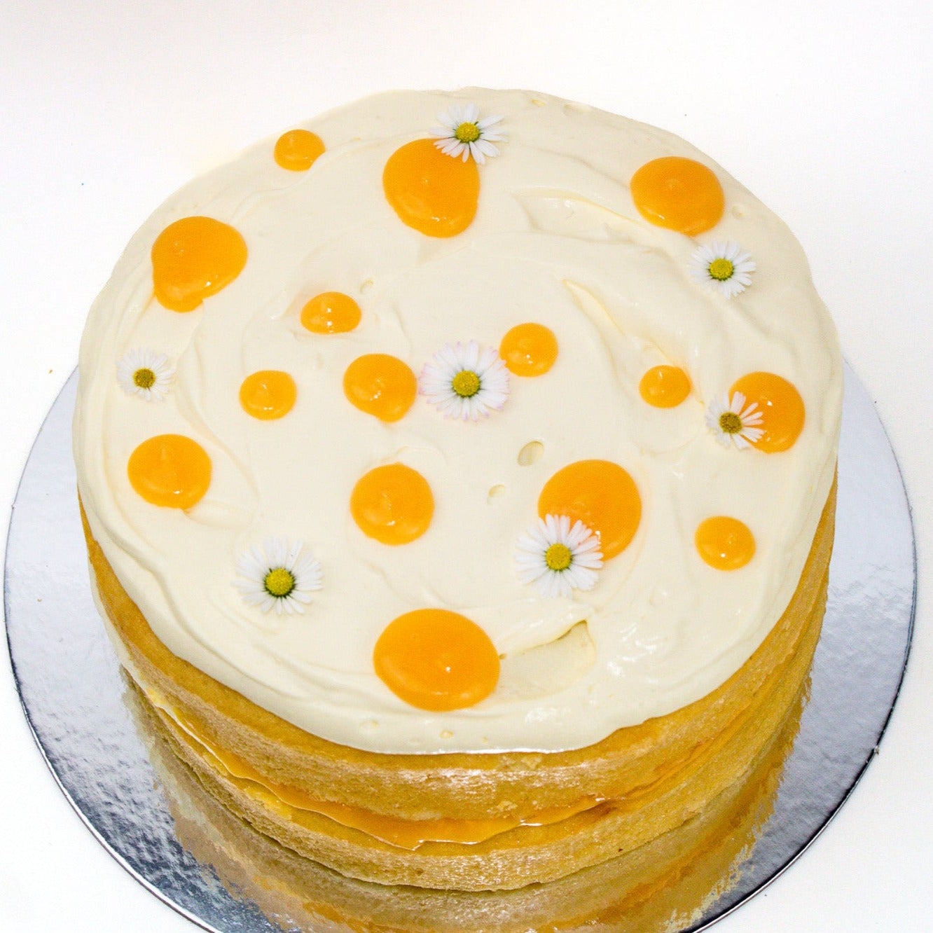 image of the top of the cake. it shows a white icing with yellow lemon curd spots and daisy's