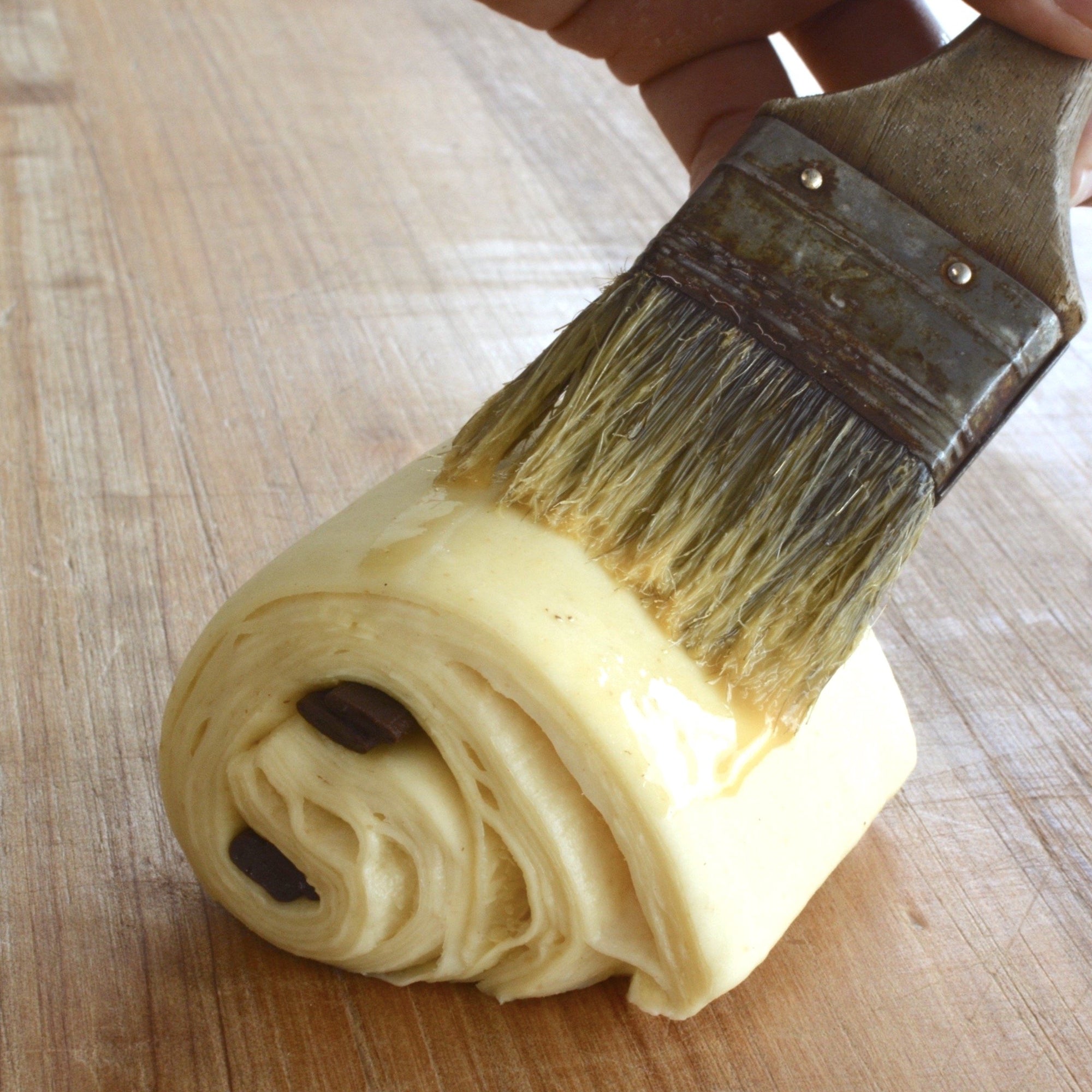 a pain au chocolat that is being egg washed using a paintbrush