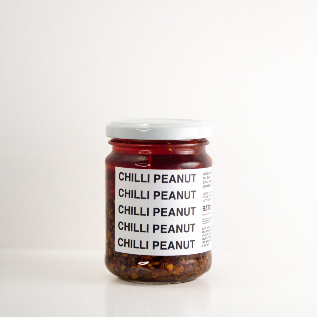 image of a clear jar with a red chilli and peanut filling. the jar has a white label with black writing and a white lid 