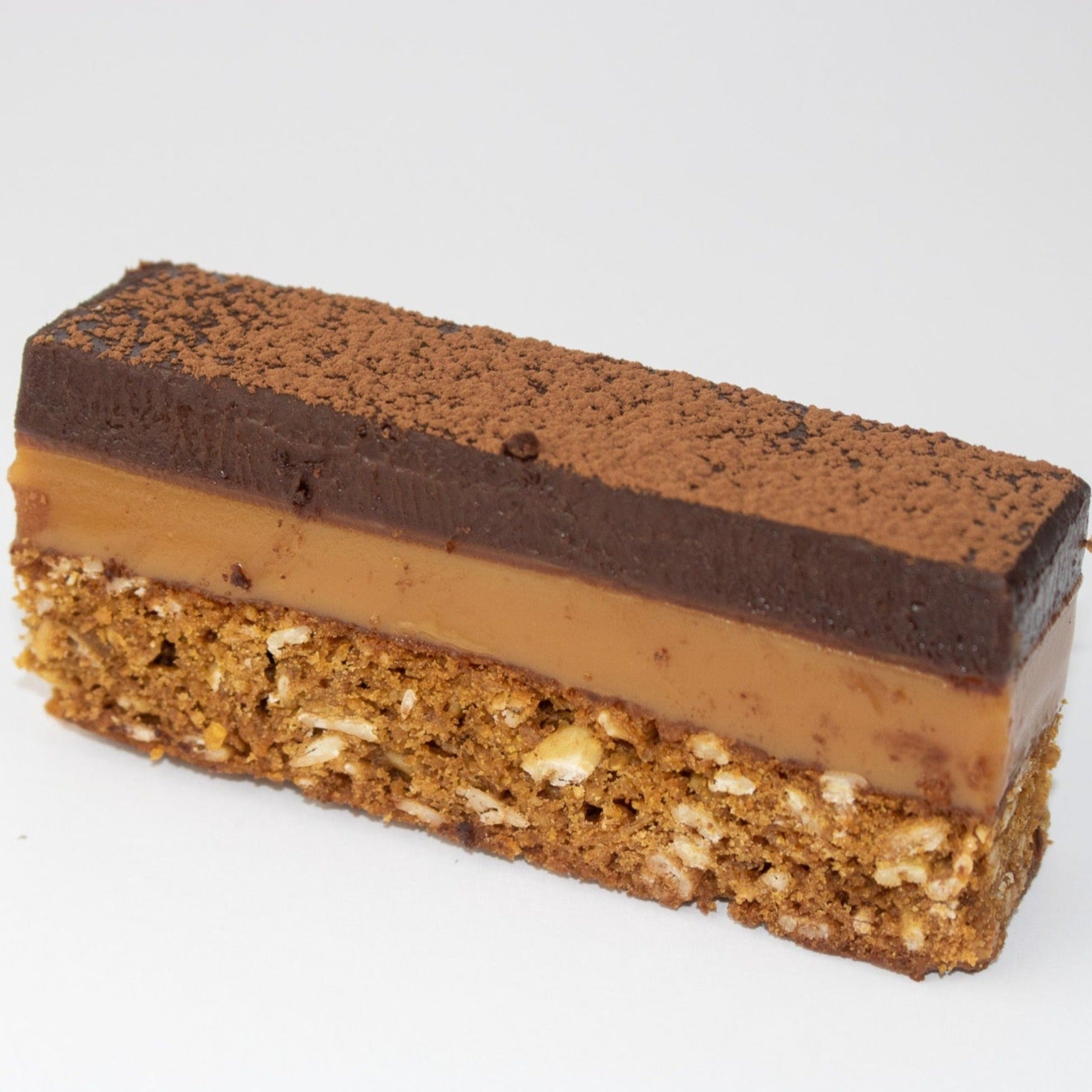 full image of a 3 layer slice. the bottom layer is an oaty biscuit. the middle layer is caramel. and at the top there is a thick layer of chocolate ganache