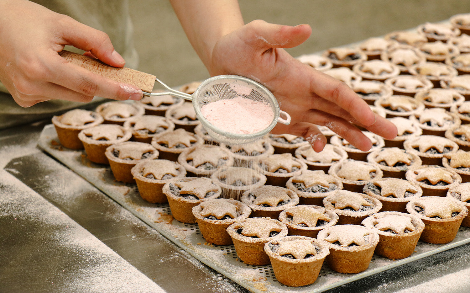 Daily Bread fruit mince pies. Person dusting mince pies with powdered sugar on a baking tray.