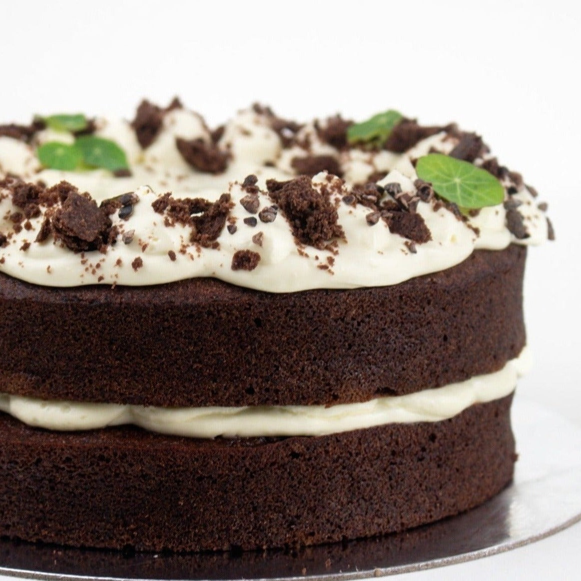 close up image of a dark chocolate cake with white icing and green leaf decoration 