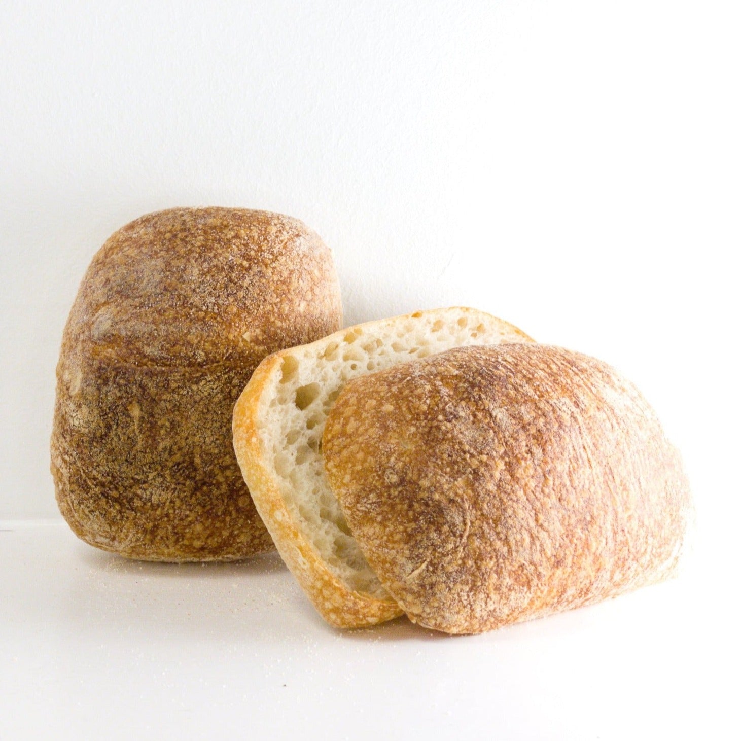 an image of two ciabatta rolls. one of the rolls is whole. the other has been sliced in half