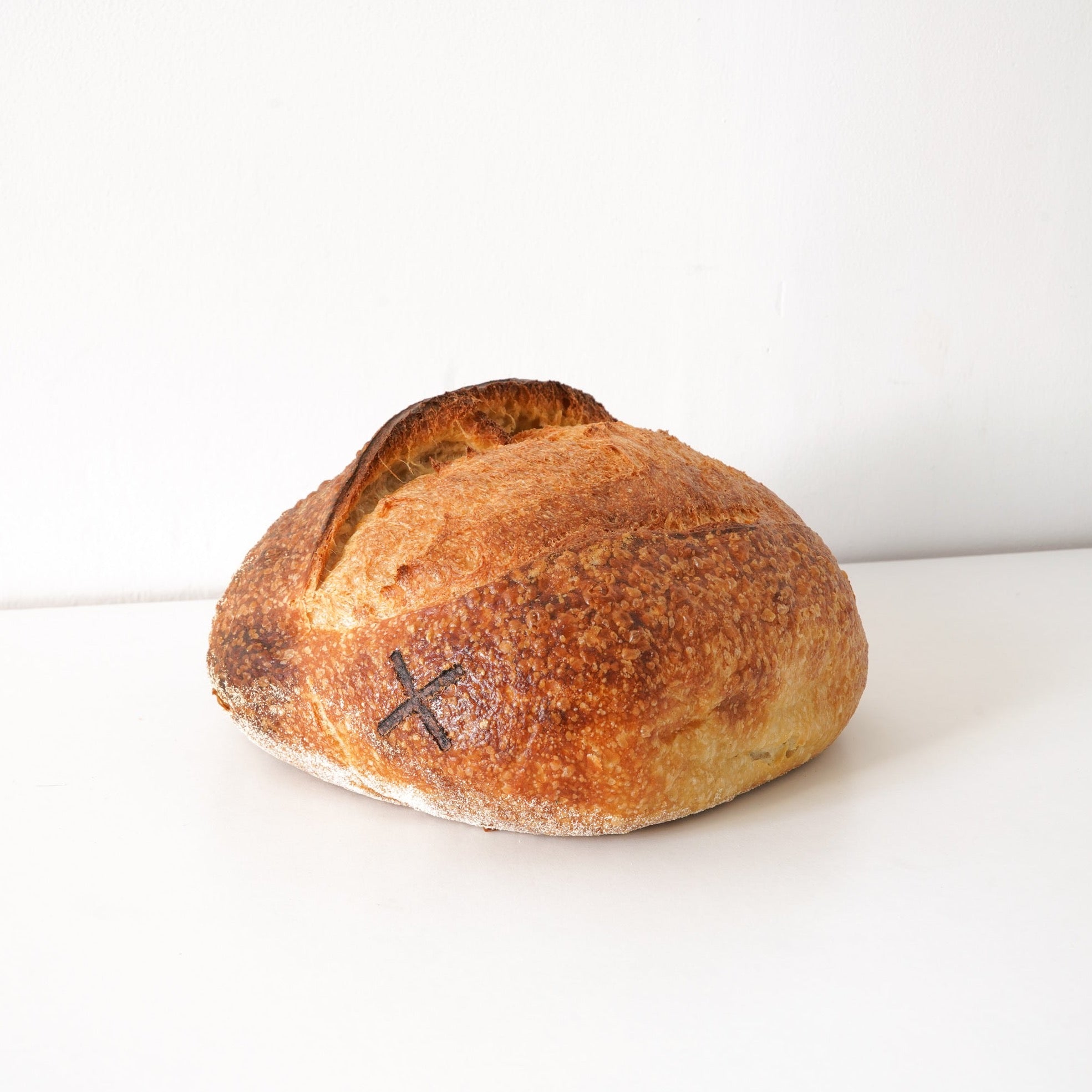 image of a dome shaped sourdough loaf of bread. the loaf has an X imprinted on it