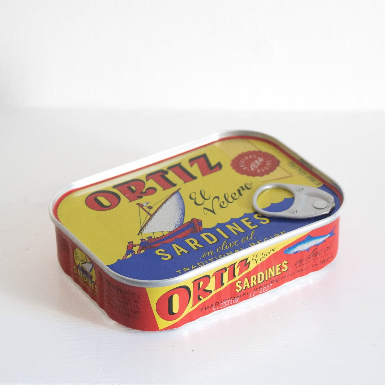 Image of a tin of sardines. the tin is yellow and blue with red and yellow writing. it also has a picture of a boat on it. 