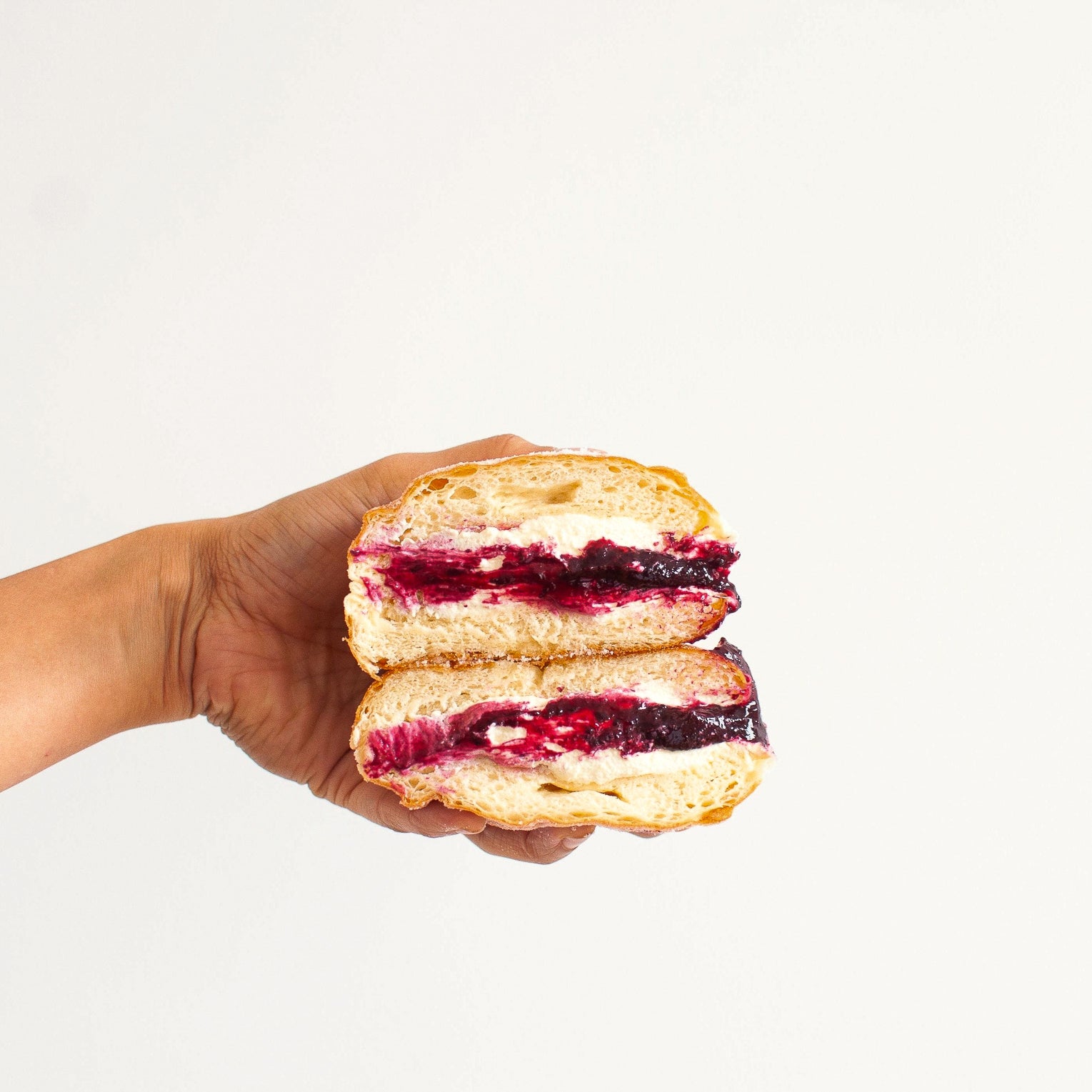 image of a hand holding a raspberry, rhubarb and cream doughnut
